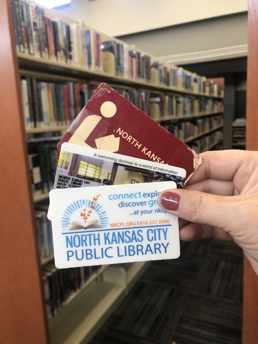 Person holding library cards in front of the bookshelves