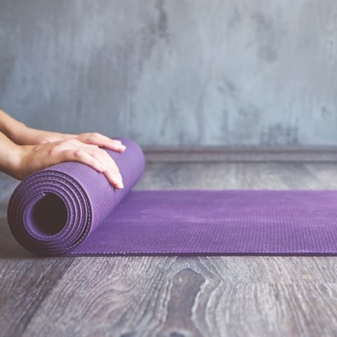 person unrolling a purple yoga mat on a grey wood floor