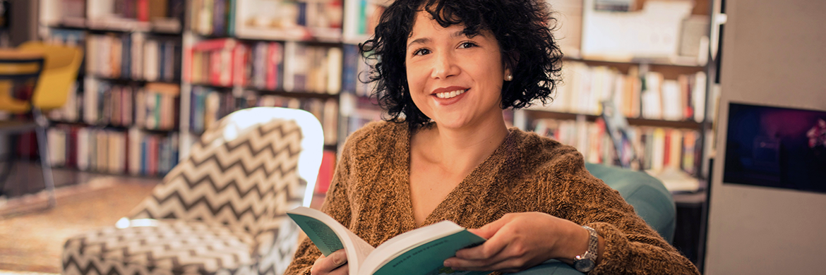 Adult woman smiling in a library with an open book in her hand